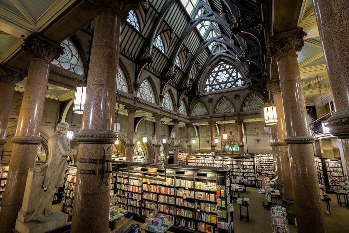 Interior grandioso de biblioteca com colunas imponentes, tetos em arco e prateleiras cheias de livros em um ambiente mágico.